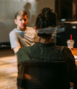 Woman sits in chair facing man.